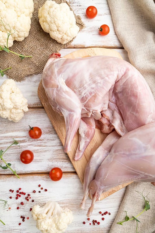 Whole raw rabbit with cauliflower, tomatoes and spices on a white wooden background and linen textile. Top view, flat lay, close up