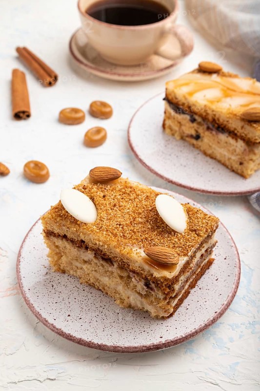 Honey cake with milk cream, caramel, almonds and a cup of coffee on a white concrete background and linen textile. Side view, close up