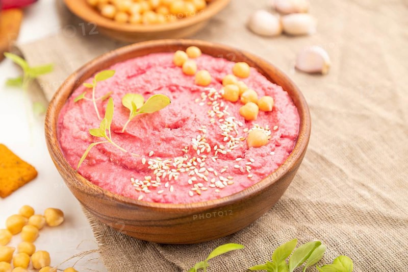 Hummus with beet and microgreen basil sprouts in wooden bowl on a white wooden background and linen textile. Side view, close up, selective focus