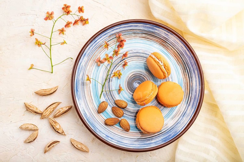 Orange macarons or macaroons cakes with cup of coffee on a white concrete background and linen textile. Top view, flat lay, close up