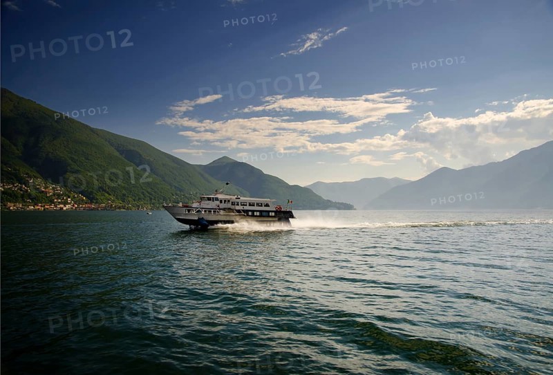 Jetfoil Passenger Ship Travel on Lake Maggiore with Mountain and Blue Sky with Clouds in a Sunny Summer Day in Piedmont, Italy, Europe