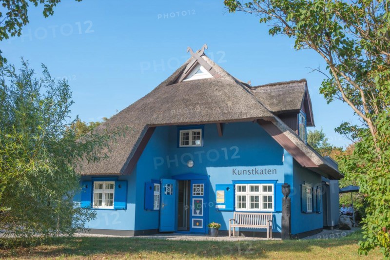 A picturesque, blue-painted thatched roof house with bench in front of the entrance, open door, horse heads on the gable, art gallery Kunstkaten under a clear, cloudless blue sky, sunny day, artist village Baltic resort Ahrenshoop, Fischland, peninsula Fischland-Darß-Zingst, Baltic Sea, Mecklenburg-Western Pomerania, Germany, Europe