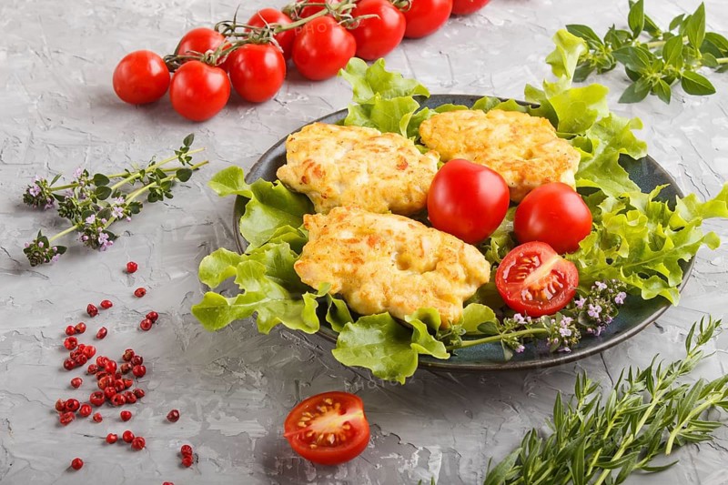 Minced chicken cutlets with lettuce, tomatoes and herbs on a gray concrete background. side view, close up