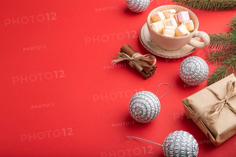 Christmas or New Year composition. Decorations, box, cinnamon, silver balls, fir and spruce branches, cup of coffee, on a red paper background. Side view, copy space