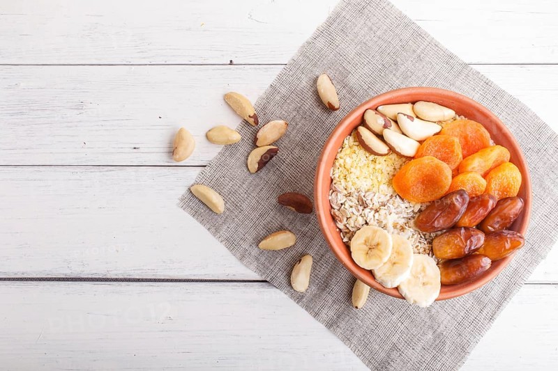 A plate with muesli, banana, dried apricots, dates, Brazil nuts on a white wooden background. top view. copy space