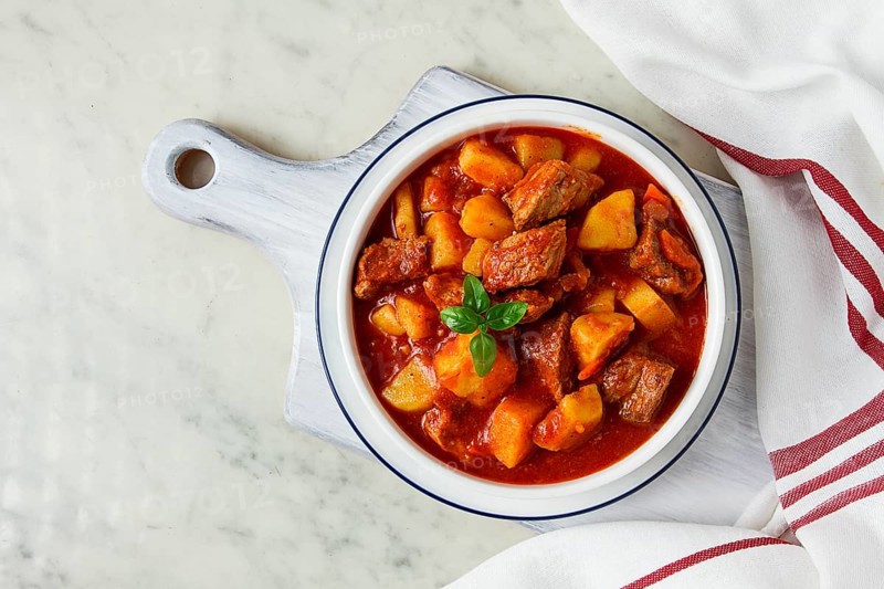 Potatoes stewed with meat, in tomato sauce, with spices and herbs, no people, on a white table