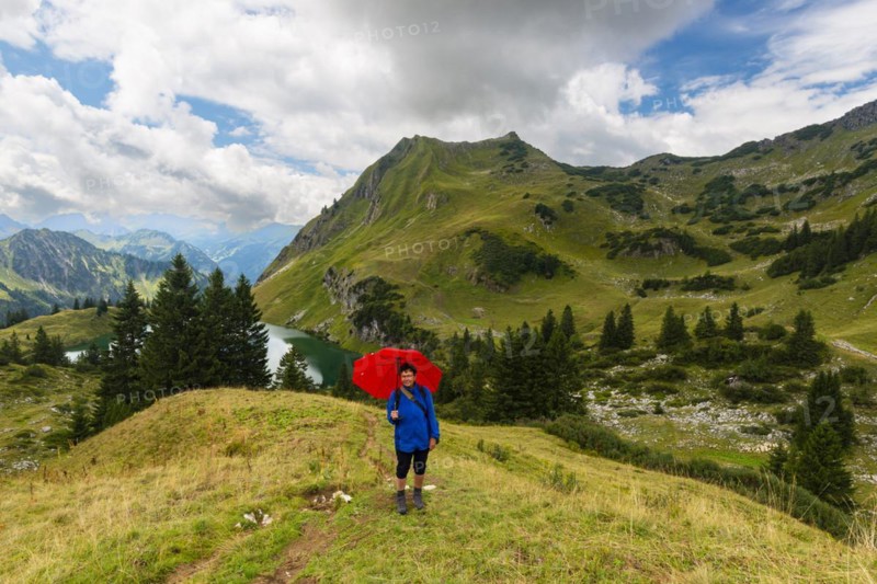Woman 60-65 hiking with umbrella, behind her Seealpsee and Seeköpfel, 1919m, Allgäu Alps, Allgäu, Bavaria, Germany, Europe
