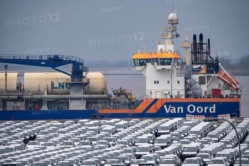 Parking space for import vehicles, hundreds of Hyundai Ioniq, electric cars, waiting for onward transport, behind them, on the Weser, the dredger, the hopper dredger, suction dredger, Vox Ariane, which holds the tug to a certain depth, at the EUROGATE container terminal in the overseas port of Bremerhaven, Lower Saxony, Germany, Europe