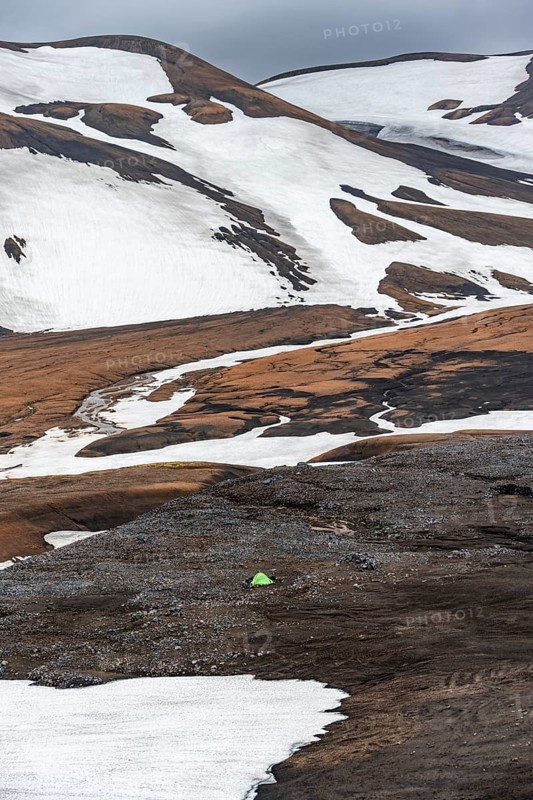 Green tent in a dramatic volcanic landscape with mountains and snow, at Höskuldsskáli hut in Hrafntinnusker, Laugavegur trekking trail, Landmannalaugar, Fjallabak Nature Reserve, Suðurland, Iceland, Europe