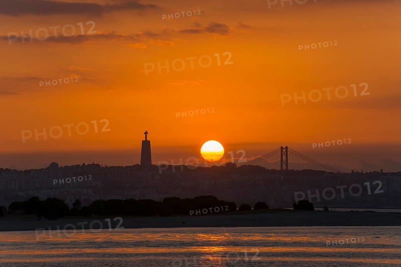 A sunset over a city by the sea with a striking statue and a bridge in the background, Statue Cristo Rei, Ponte 25 de Abril, Bridge of 25 April, Suspension bridge over the Tagus, Lisbon, Lisboa, Portugal, Europe