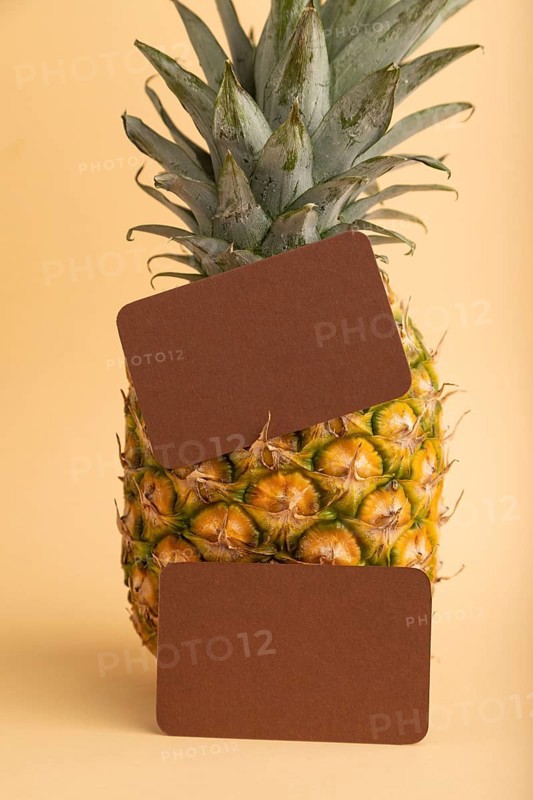 Brown paper business card with ripe pineapple on orange pastel background. Side view, copy space. Tropical, healthy food, vacation, holidays concept