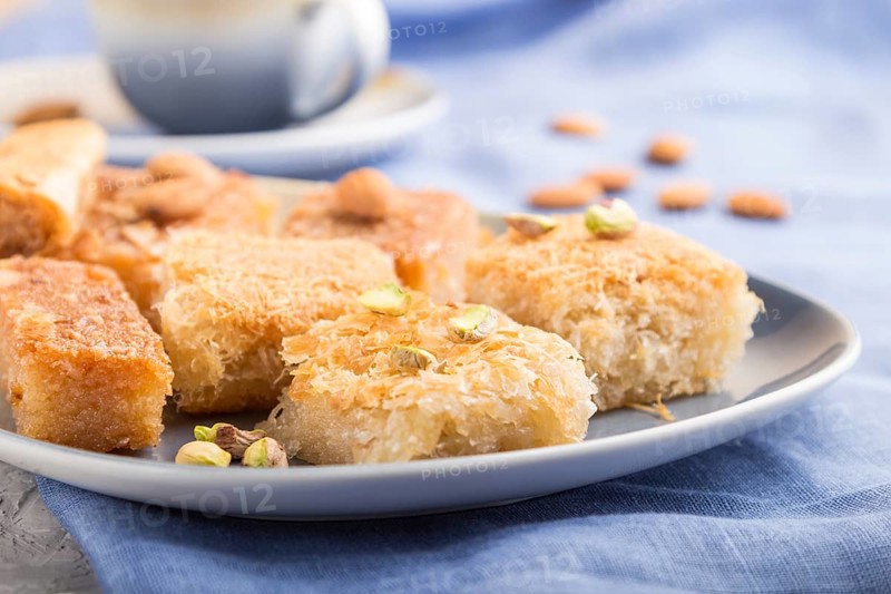 Traditional arabic sweets (basbus, kunafa, baklava) and a cup of coffee on a gray concrete background and blue textile. side view, close up, selective focus