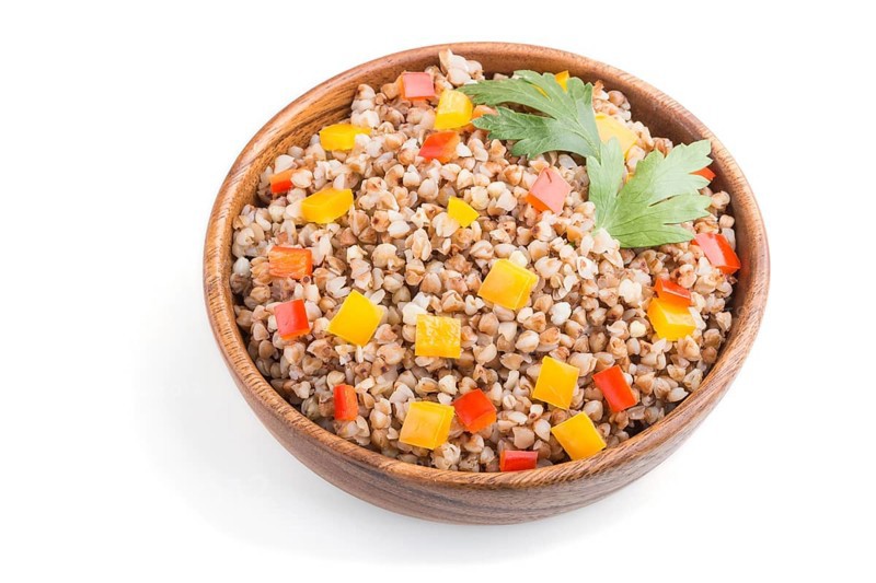 Buckwheat porridge with vegetables in wooden bowl isolated on white background. Side view, close up. Russian traditional cuisine