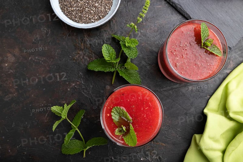 Watermelon juice with chia seeds and mint in glass on a black concrete background with green textile. Healthy drink concept. Top view, close up, flat lay