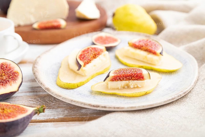 Summer appetizer with pear, cottage cheese, figs and honey on a white wooden background and linen textile. Side view, close up, selective focus