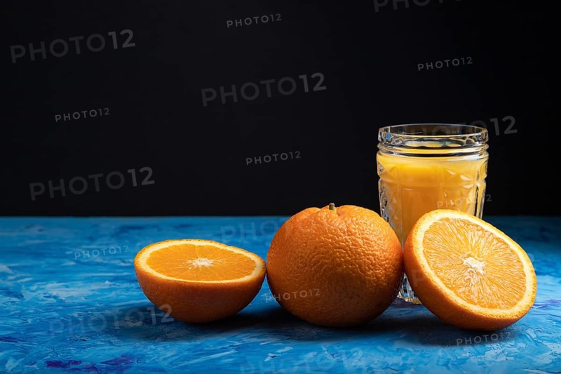 Glass of orange juice on a black and blue background. Hard light, contrast. Side view, copy space