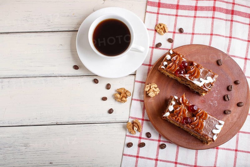 A piece of cake with caramel cream on a wooden kitchen board and a cup of coffee, white background, top view, flat lay, copy space