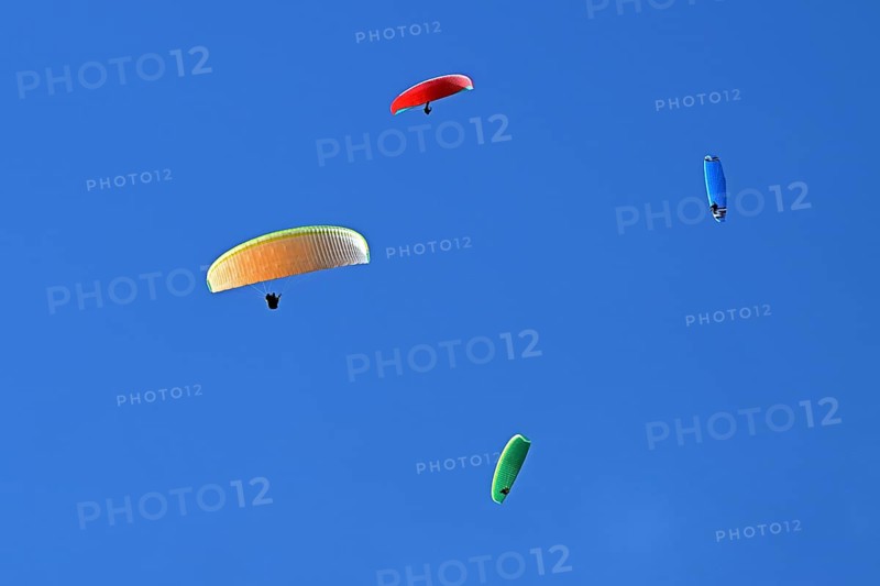 Four colourful paragliders fly in the blue sky