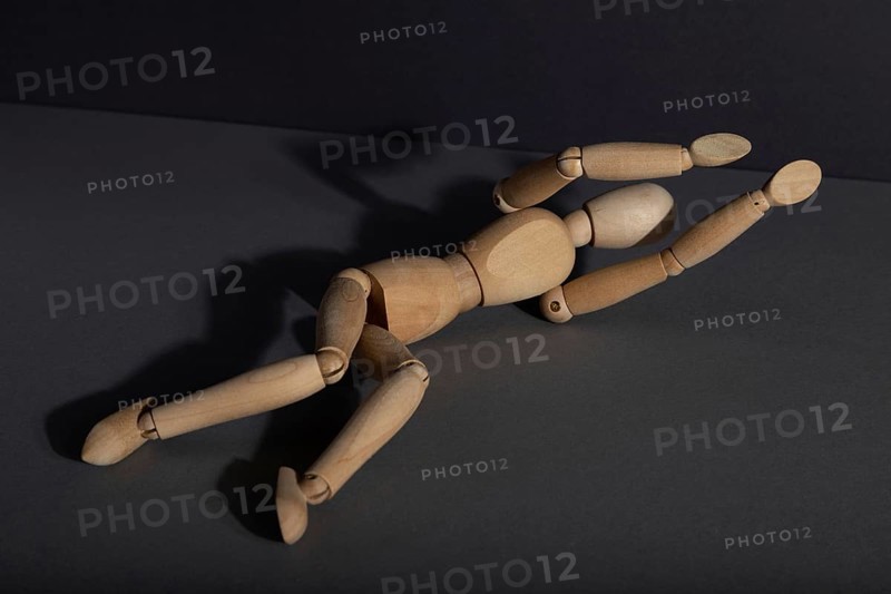 Wooden mannequin lies in a protective position on gray background. loneliness, violence, vulnerability, depression disorder concept. copy space, hard light