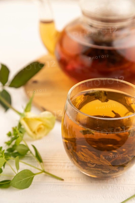 Red tea with herbs in glass teapot on white wooden background. Healthy drink concept. Top view, close up, selective focus