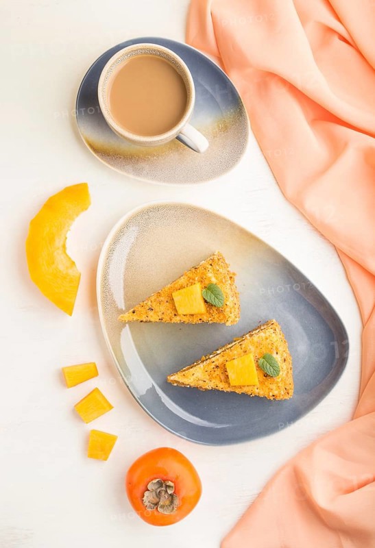 Homemade cake with persimmon and pumpkin and a cup of coffee on a white wooden background with orange textile. top view, flat lay, close up