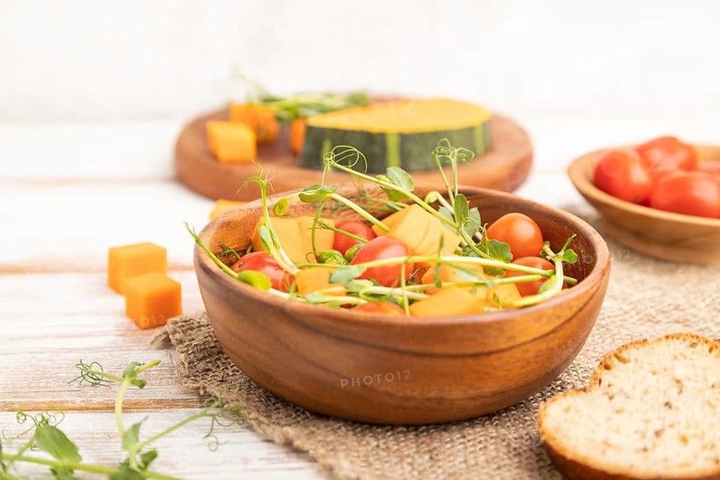 Vegetarian vegetable salad of tomatoes, pumpkin, microgreen pea sprouts on white wooden background and linen textile. Side view, close up, selective focus