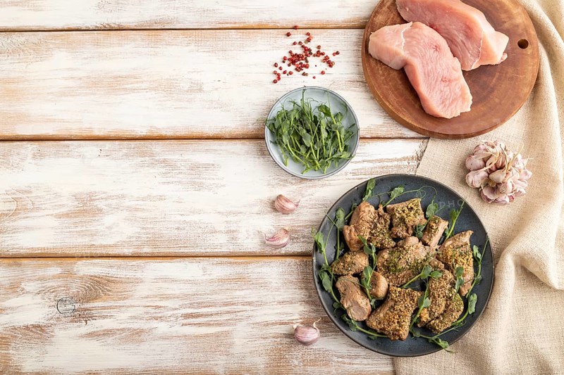 Stewed turkey fillet with garlic and sprouts of green peas on white wooden background and linen textile. Top view, flat lay, copy space