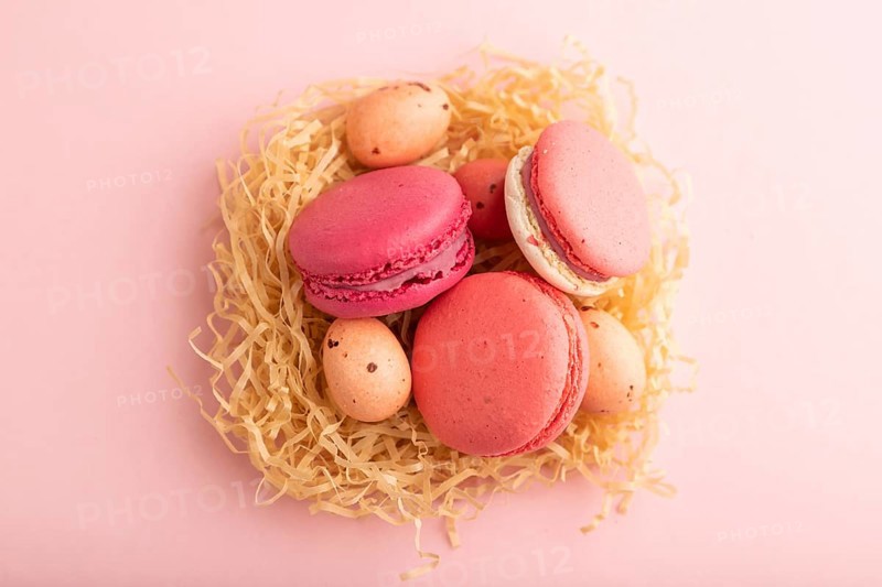 Purple and pink macaroons and chocolate eggs in decorative paper nest on pink pastel background. top view, flat lay, close up, still life. Breakfast, morning, easter concept