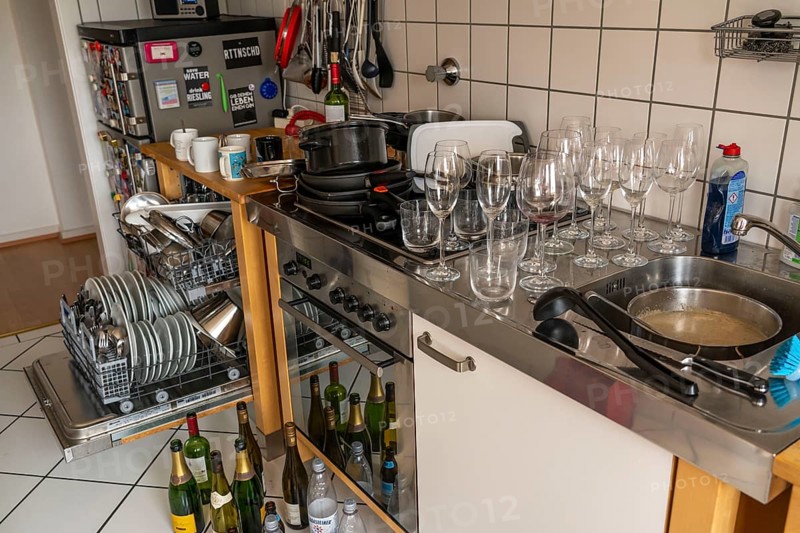 Kitchen after a big dinner, cooking party, dishwasher, full, with cleaned dishes, dirty glasses, pots, cooking utensils on the sink, waiting to be washed