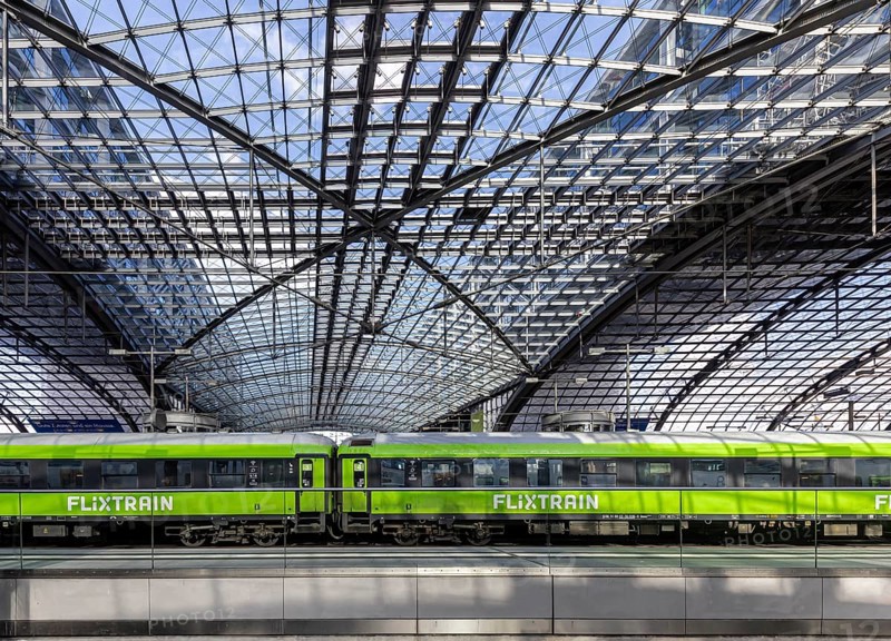 Central station, pillarless glass roof construction above the platforms, green train of the railway company Flixtrain. Berlin, Germany, Europe
