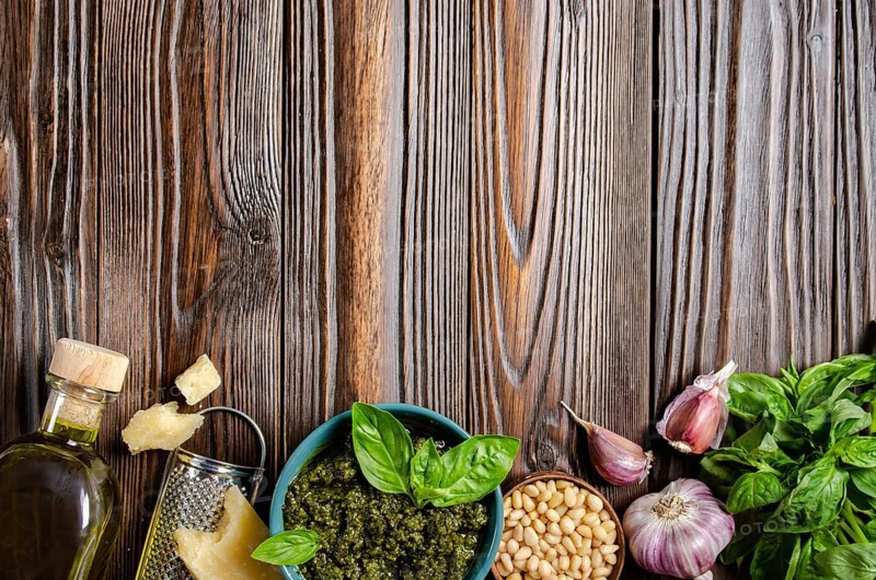 Flat lay food background of genovese pesto sauce and its ingredients on wooden kitchen table with copy-space