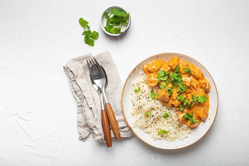 Traditional Indian dish chicken curry with basmati rice and fresh cilantro on rustic white plate on white concrete table background from above. Indian dinner meal, food photography