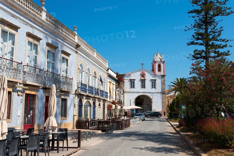 Cosy street lined with buildings and cafés, in the background a church under a clear sky, on the left houses with azulejos, in the background Igreja de Nossa Senhora da Ajuda ou de São Paulo, Church of Our Lady of Help or São Paulo, Praça Dr António Padinha, Tavira, Faro, Algarve, Portugal, Europe