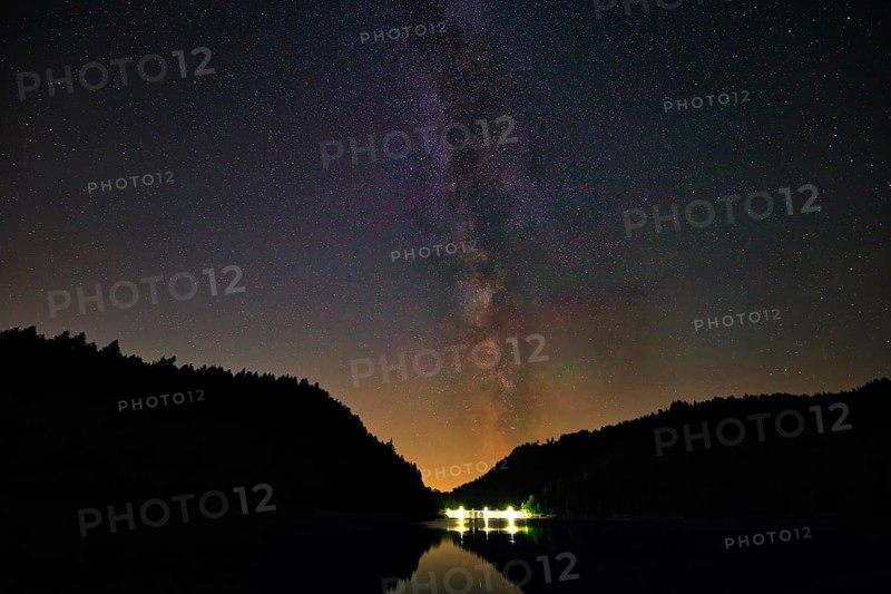 The Milky Way stretches across the night sky over a calm lake, framed by dark trees, Alp Stausee, Sankt Blasien, Black Forest, Baden- Württemberg, Germany, Europe