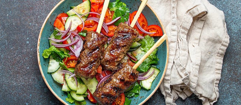 Grilled skewer meat beef kebabs on sticks served with fresh vegetables salad on plate on rustic concrete background from above. Traditional Middle Eastern and Turkish dish Kebab, food photography