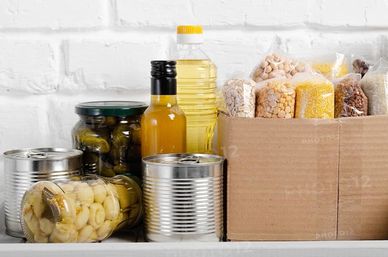 Set of uncooked foods on pantry shelf prepared for disaster emergency conditions on brick wall background closeup view