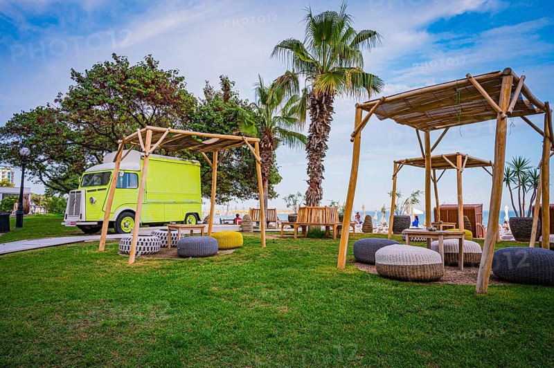 A yellow motorhome next to wooden canopies and palm trees on a green meadow near the sea, Golden Sands, Varna, Bulgaria, Europe
