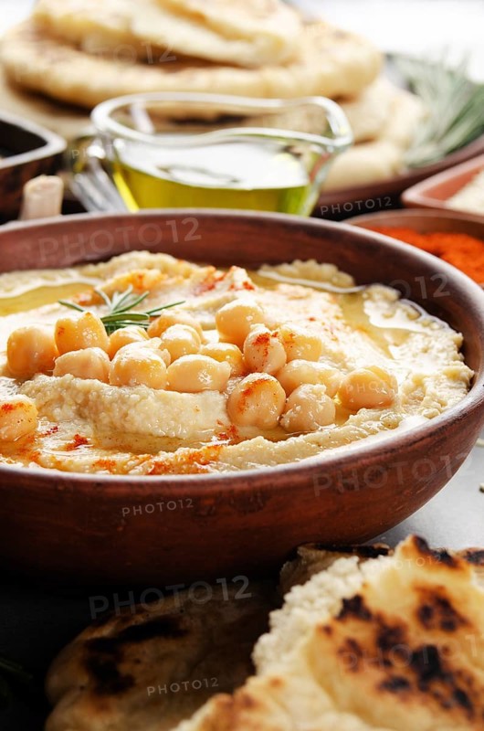 Low angle view at Hummus topped with chickpeas, olive oil and green coriander leaves on stone table with pita bread and spices aside