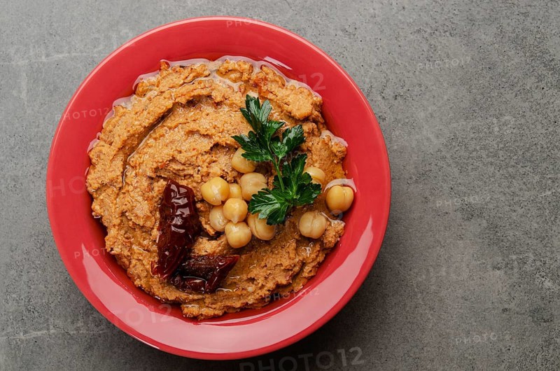 Flat lay view at hummus topped with chickpeas, sun dried tomatoes and green coriander leaves on stone table