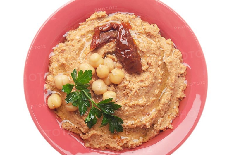Flat lay view at hummus topped with beans, sun dried tomatoes and green coriander leaves isolated on white background. Clipping path added