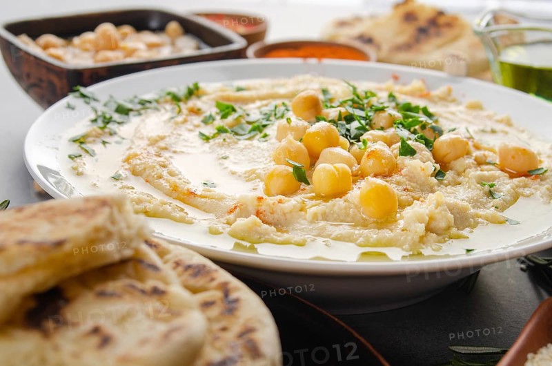 Closeup view at Hummus topped with beans olive oil and green coriander leaves on kitchen table with pita bread