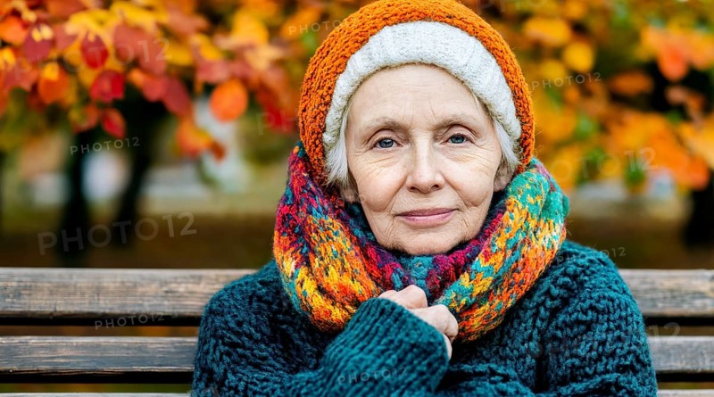 Senior citizen with colourful knitted hat and scarf sits warmly wrapped up on a bench in autumn, generated with AI, AI generated
