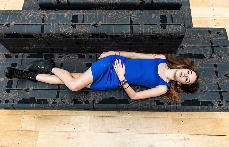 Portrait of an 18 year old white woman, in a blue short dress, lying on a grey couch, view from above, Brussels