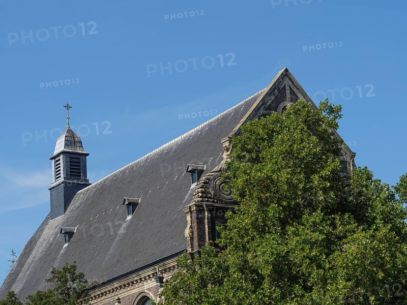 Historic church building, partly covered by trees under a blue sky, maastricht. netherlands