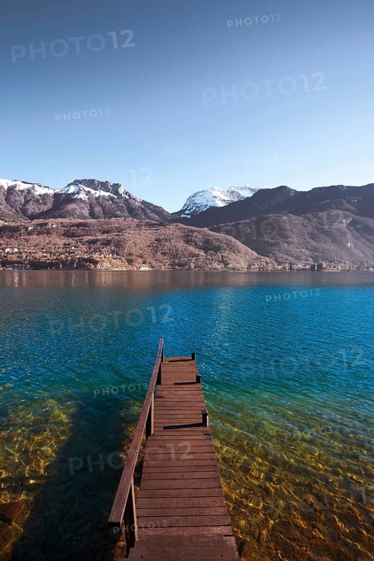An old wooden pier faces the snow-capped mountains of the French alps on beautiful Lake Annecy. Vertical