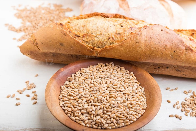 Fresh baked bread and wooden plate with wheat seeds on a white wooden background. side view, close up