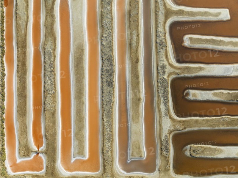 Saline ponds at the salt works near Chiclana de la Frontera. The orange-red colour depends on the level of salinity and is directly caused by the algae Dunaliella salina and brine shrimp. Aerial view. Drone shot. Cádiz province, Andalusia, Spain, Europe