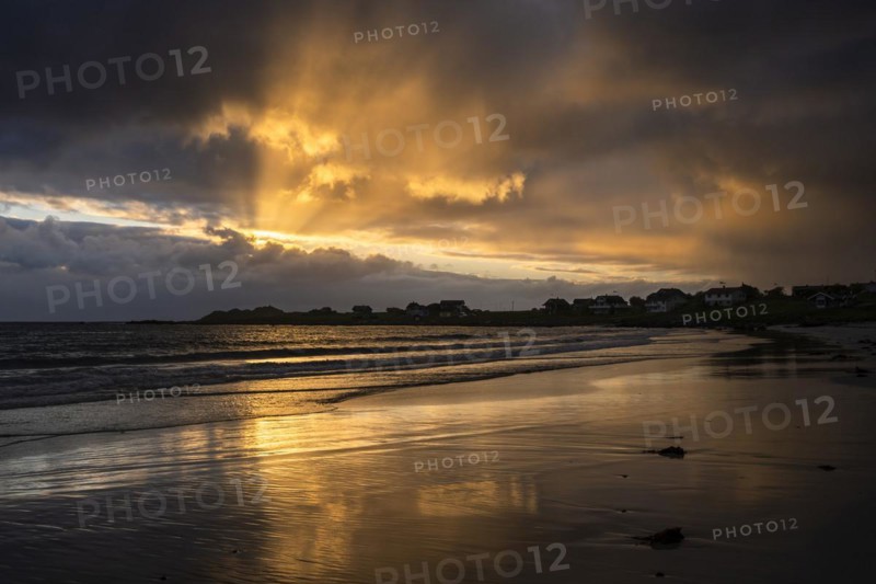 Landscape on the Lofoten Islands. The village of Ramberg, with the sea and the sandy beach (Rambergstranda) in front of it. Dramatic sky with clouds and sunbeams. Reflection. At night at the time of the midnight sun. Early summer. Ramberg, Flakstadoya, Lofoten, Norway, Europe
