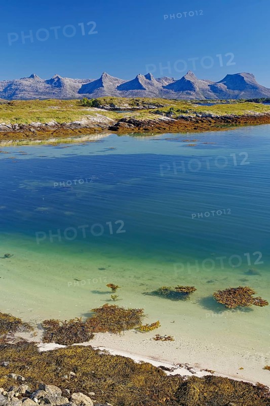 A calm, clear fjord with seaweed, white sandy beach and mountains in the background under a bright blue sky, Seven Sisters mountain range, Alstahaug, Nordland, Norway, Europe