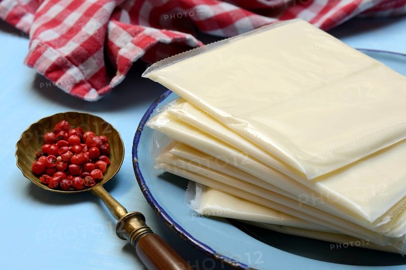 Processed cheese, slices of processed cheese wrapped in plastic and spoon with pink berries, red pepper
